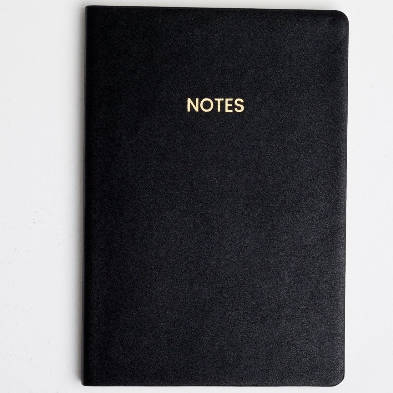 A black colored vegan leather notebook with gold foil text reading &quot;NOTES&quot; across the front photographed against a white background.