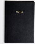 A black colored vegan leather notebook with gold foil text reading "NOTES" across the front photographed against a white background.
