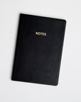 A black colored vegan leather notebook with gold foil text reading "NOTES" across the front photographed against a white background.