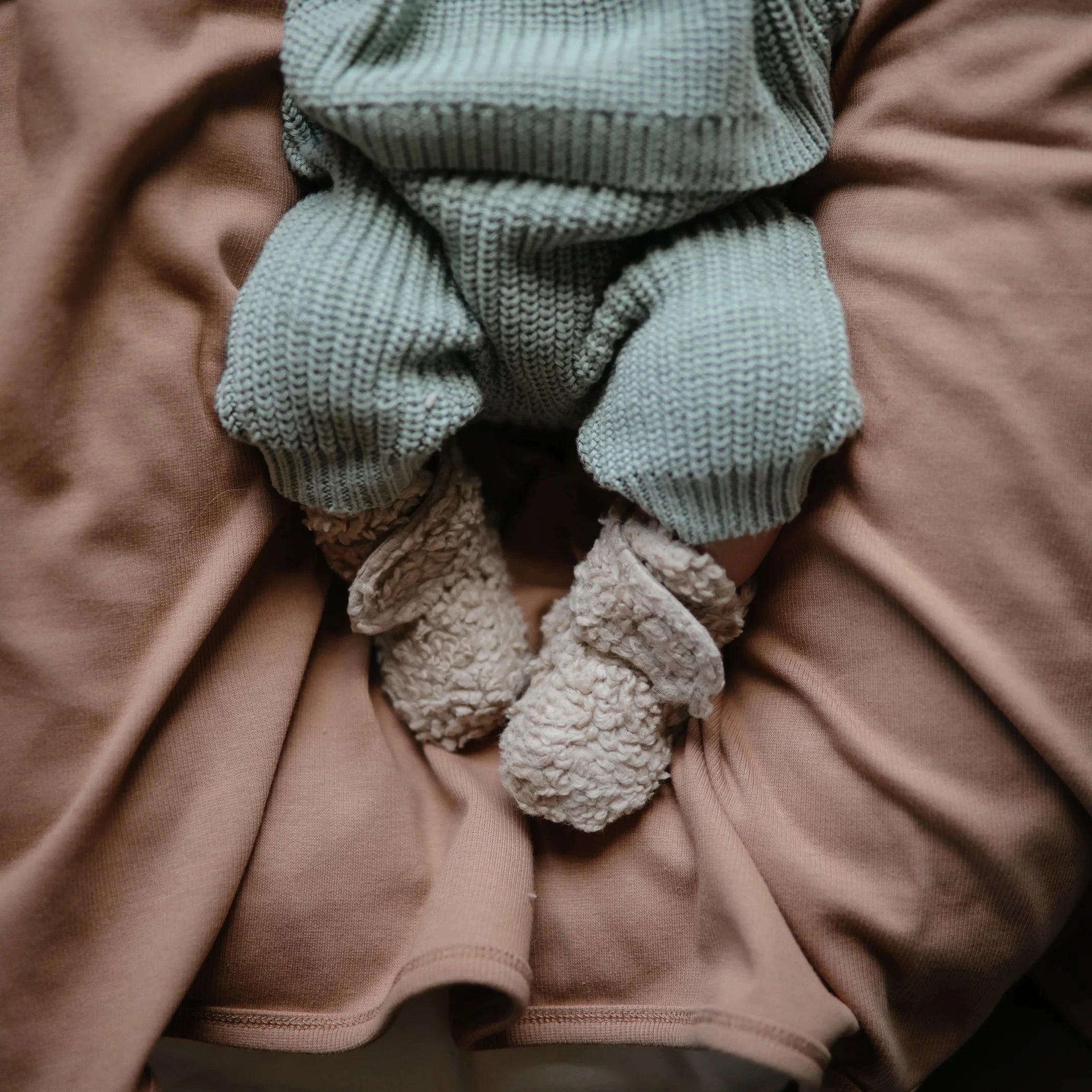 baby laying on mauve blanket with brown booties on. baby is wearing green knitted two piece set