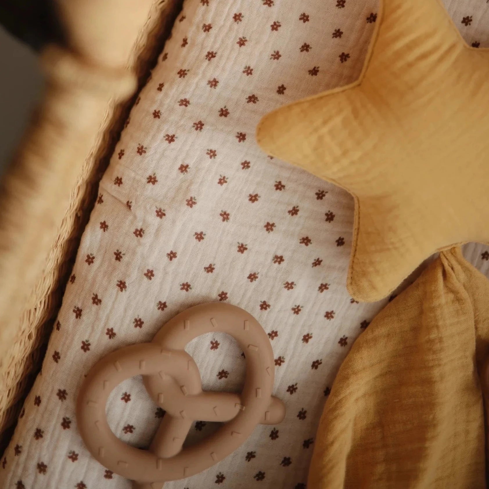 Pretzel teether inside crib with yellow blanket next to it and a star shaped cushion