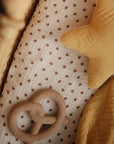 Pretzel teether inside crib with yellow blanket next to it and a star shaped cushion