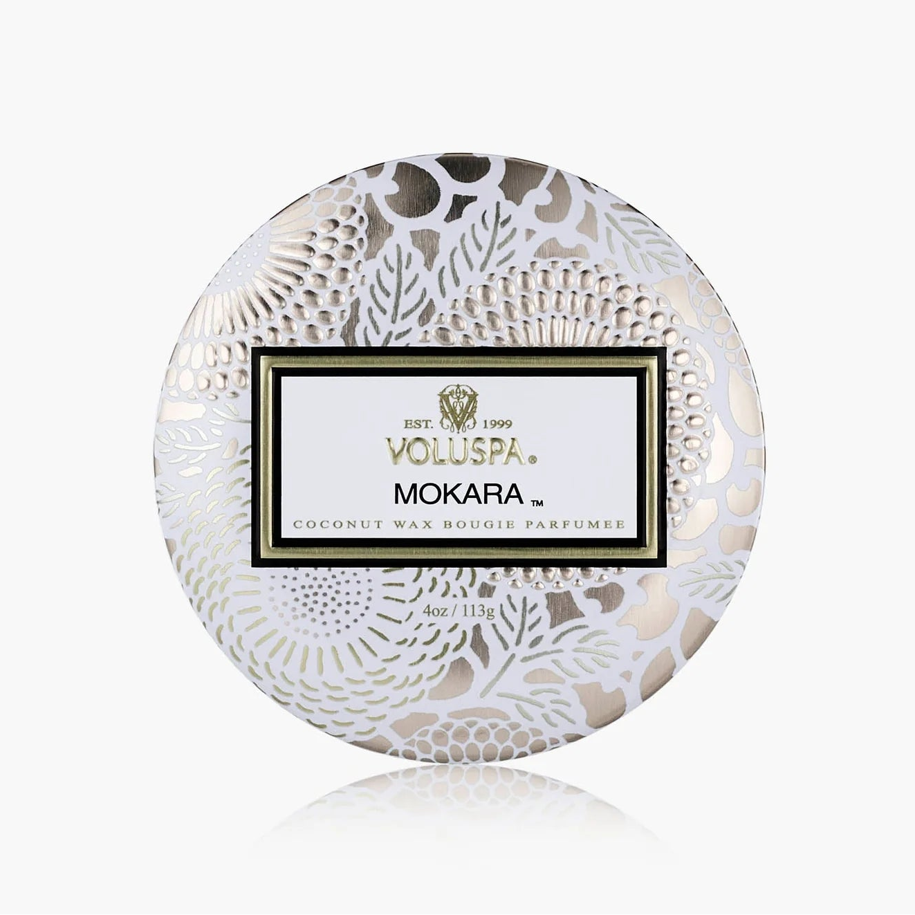A round decorative box for a Voluspa Mokara coconut wax melt perfume, featuring a white and silver floral lace pattern with a central white label.