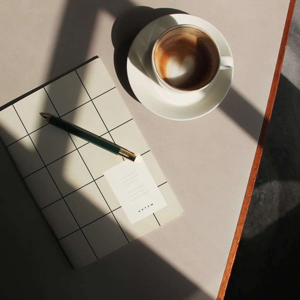 Milo Weekly Planner | Light Gray Grid next to cup of coffee and pen