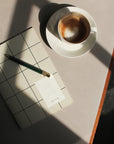 Milo Weekly Planner | Light Gray Grid next to cup of coffee and pen