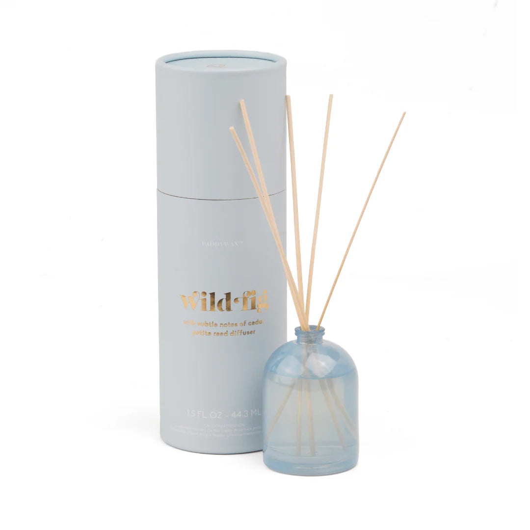 A reed diffuser set with a light blue glass bottle, natural reed sticks, and a pale gray cylindrical box with gold 'wild-fla' lettering, photographed on a white background.