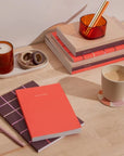 Tangerine Concept Planner on desk with other planners, notebooks, mug, candle, pens, etc.