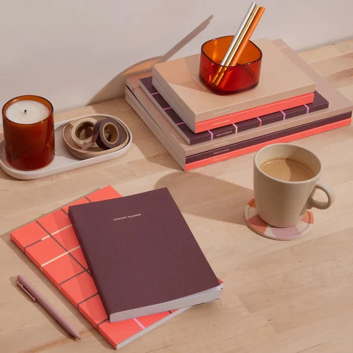 Maroon Concept Planner on desk surrounded by notebooks, pens, mugs, etc