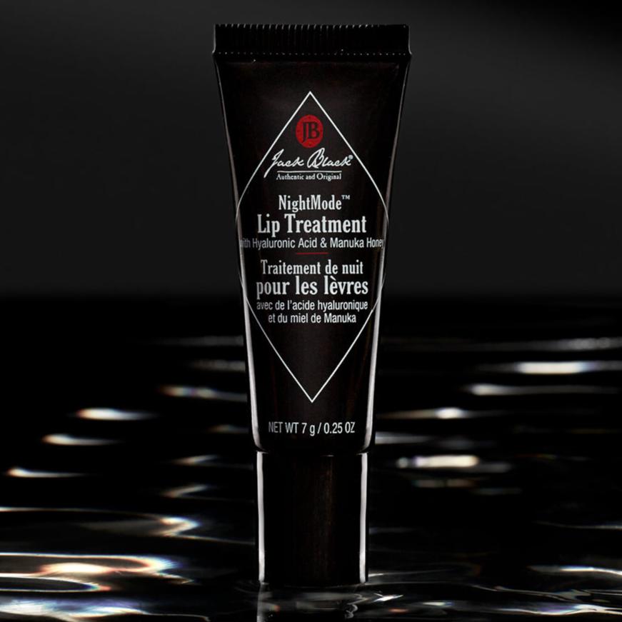 Black tube labeled "Jack Black NightMode Lip Treatment" with text "with Hyaluronic Acid & Manuka Honey" and "NET WT 7 g / 0.25 OZ" in white, on a black background. Product claims to hydrate and nourish lips overnight.