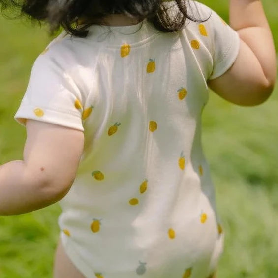 baby walking through field wearing lemon tree one piece 