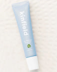 A light blue squeeze tube with white cap and white text reading, "kinfield Lip Rescue Repair Balm". Photographed on white background.