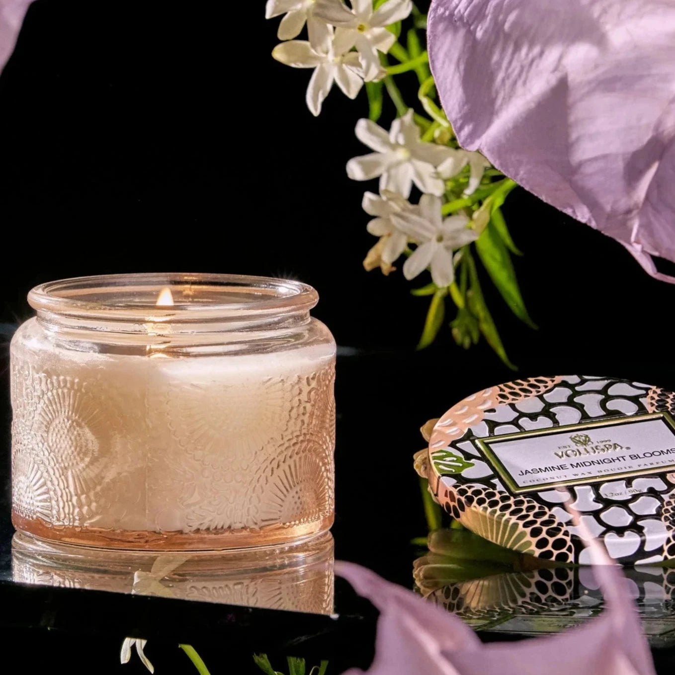 pale pink candle surrounded by flowers on a black background