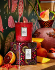 Red candle with decorative box on a wooden surface with fruits and flowers.