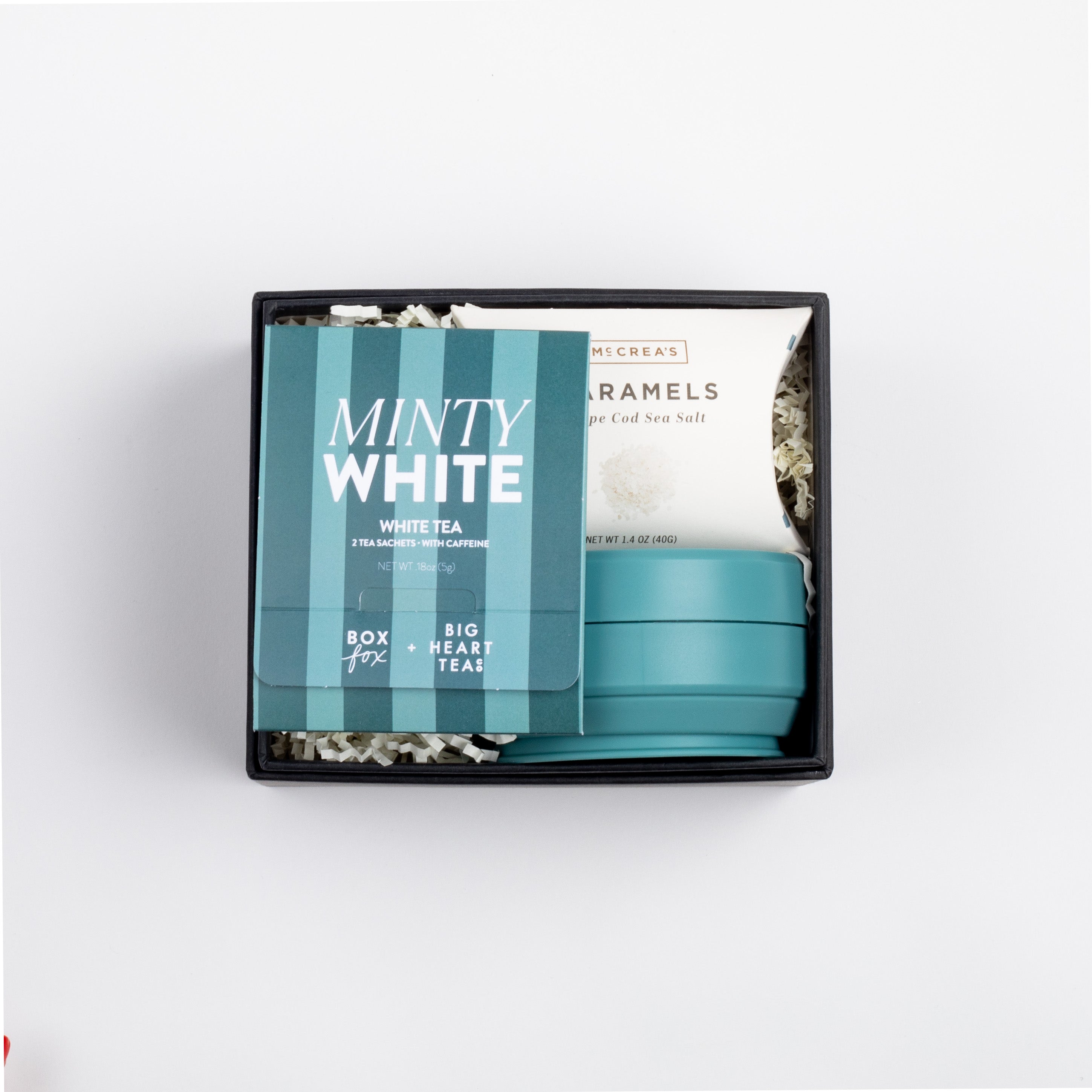 Black BOXFOX box open with white tea sachet, sea salt caramels and a teal stojo bottle shown closed.