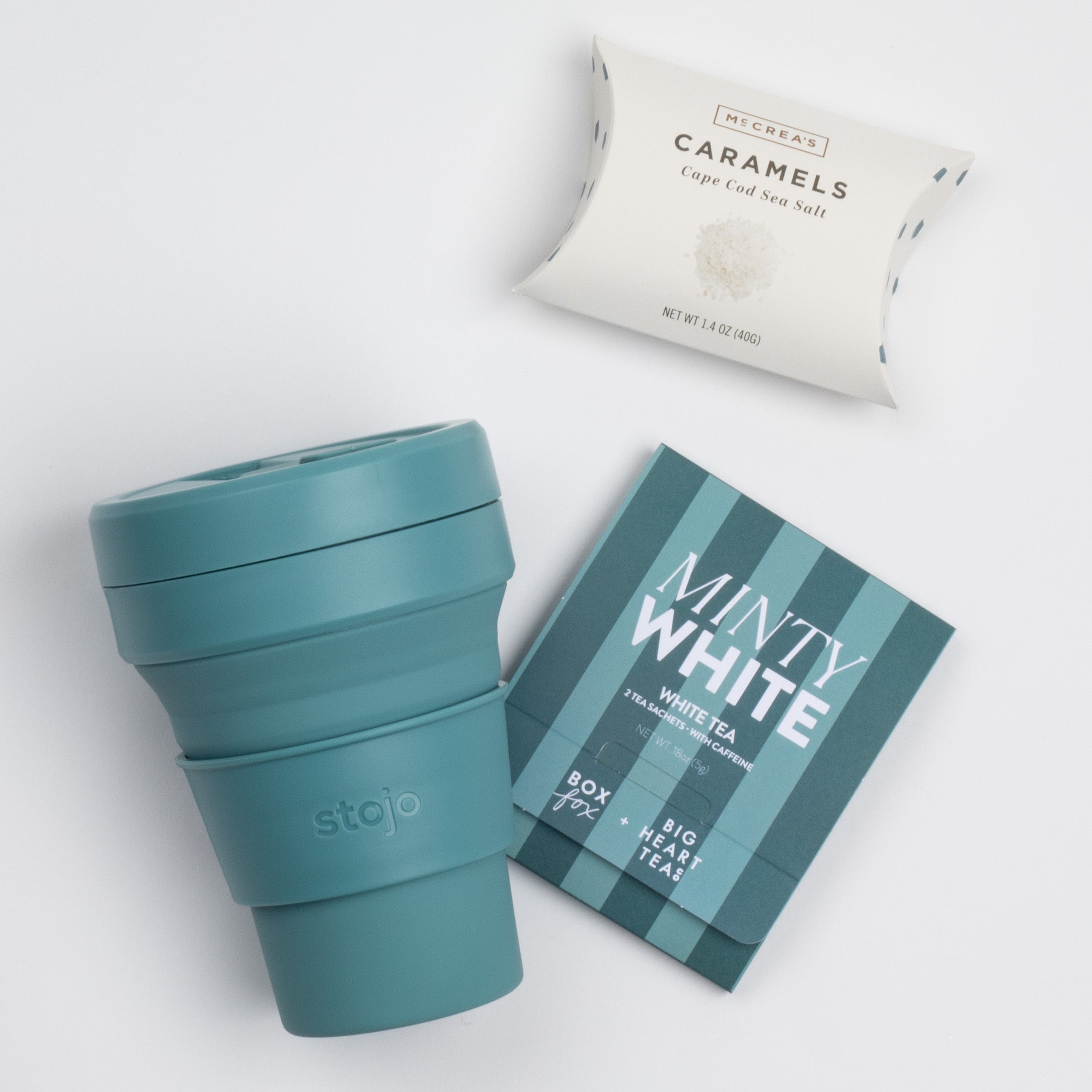 The inside of the SNOW ON THE BEACH curated box: white tea sachet, sea salt caramels and a teal stojo bottle shown open.