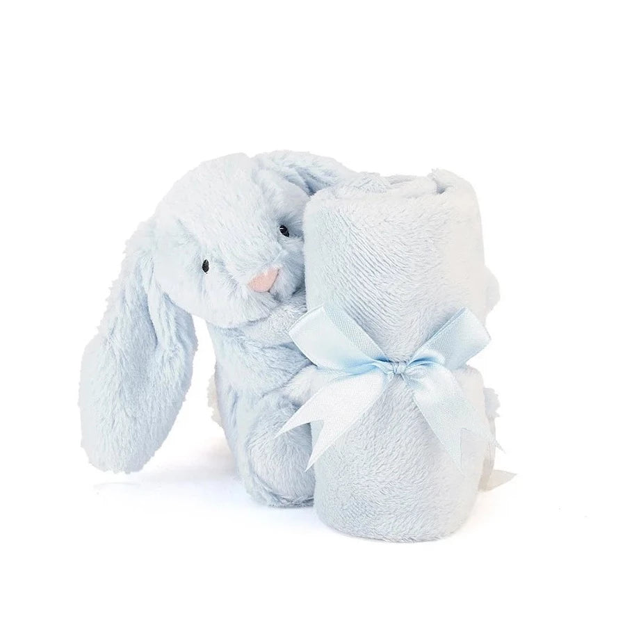 pale blue stuffed bunny with small blanket rolled iiin front of it. Looks like the bunny is holding blanket. blanket has blue bow tied on it