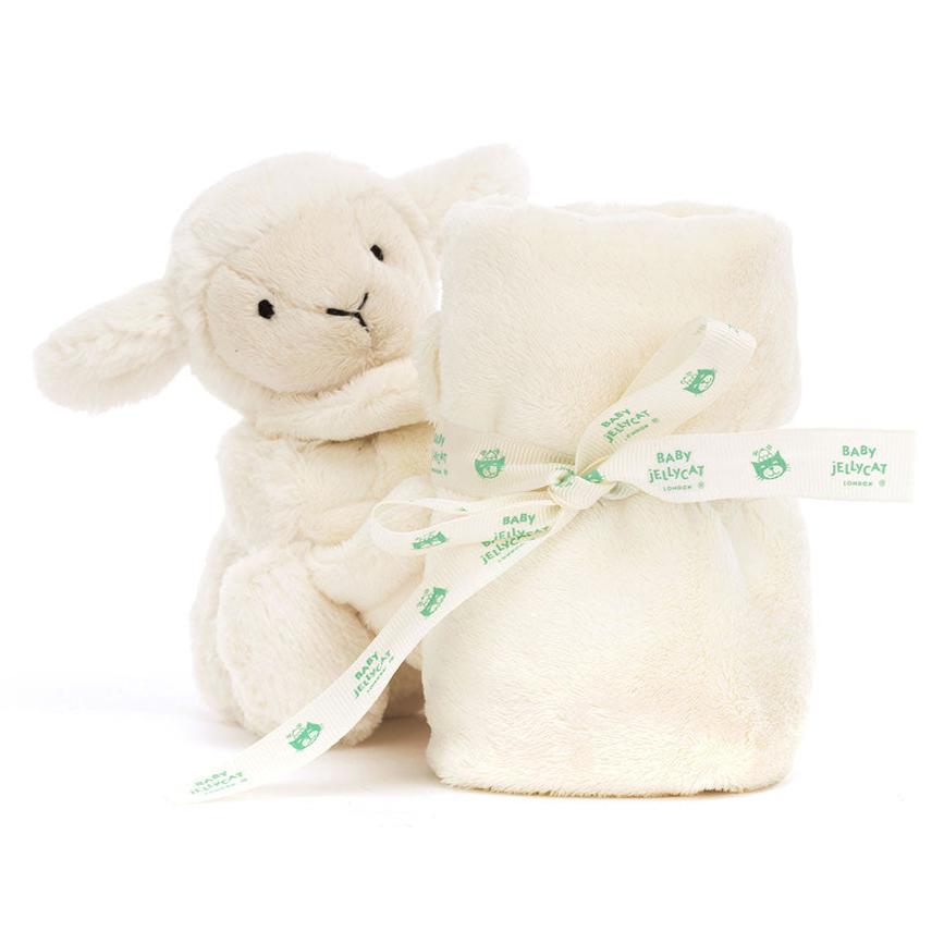 cream stuffed lamb with small blanket rolled in front of it. Looks like the lamb is holding blanket. blanket has cream jellycat bow tied on it