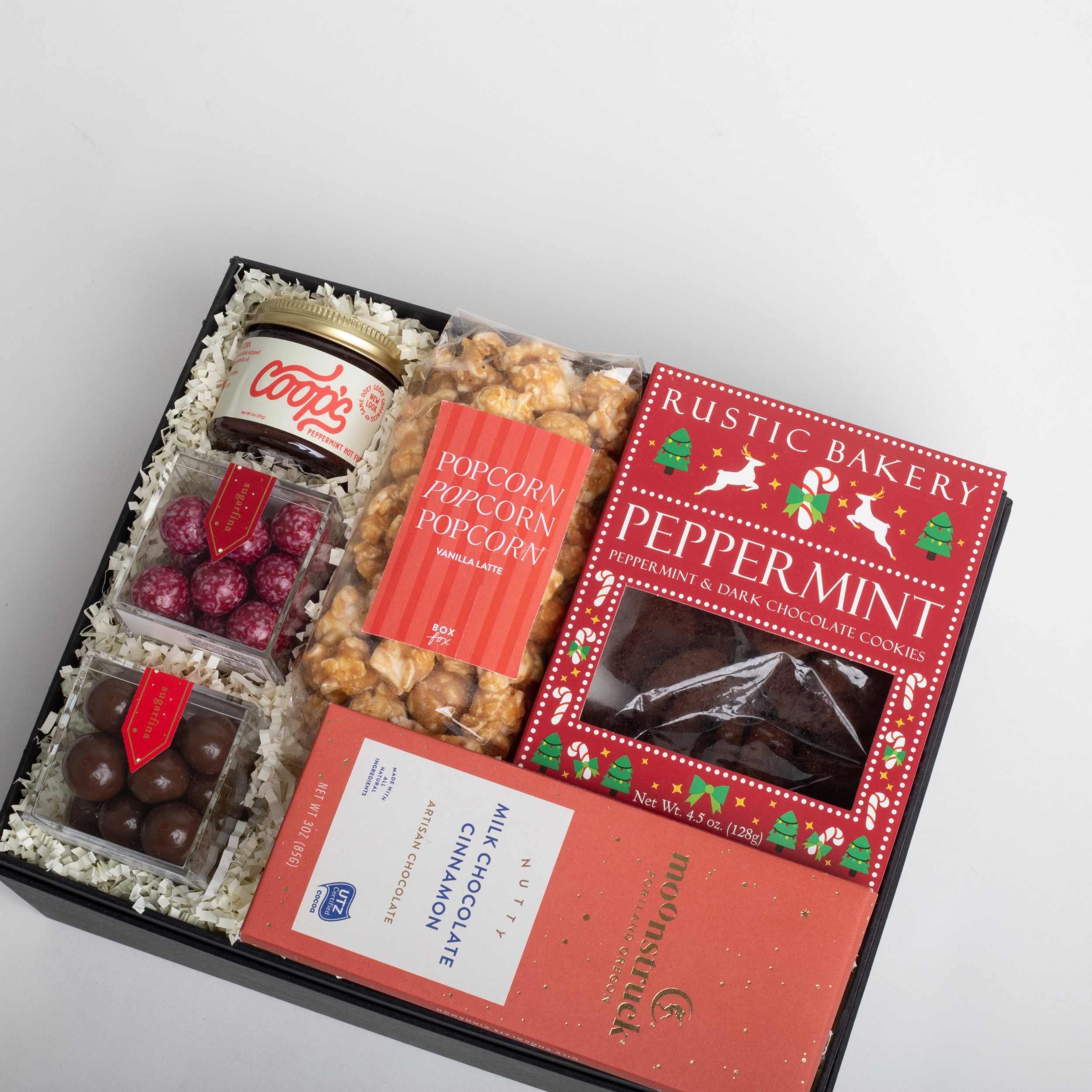 Gift box with Christmas-themed treats including peppermint cookies and popcorn.