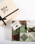 A luxury gourmet gift box set from Box Fox, featuring a cream-colored gift box with a black ribbon and a tray of assorted gourmet snacks including caramel-coated chocolates, popcorn, dried cranberries, and Twinkles, arranged on a clean white background.