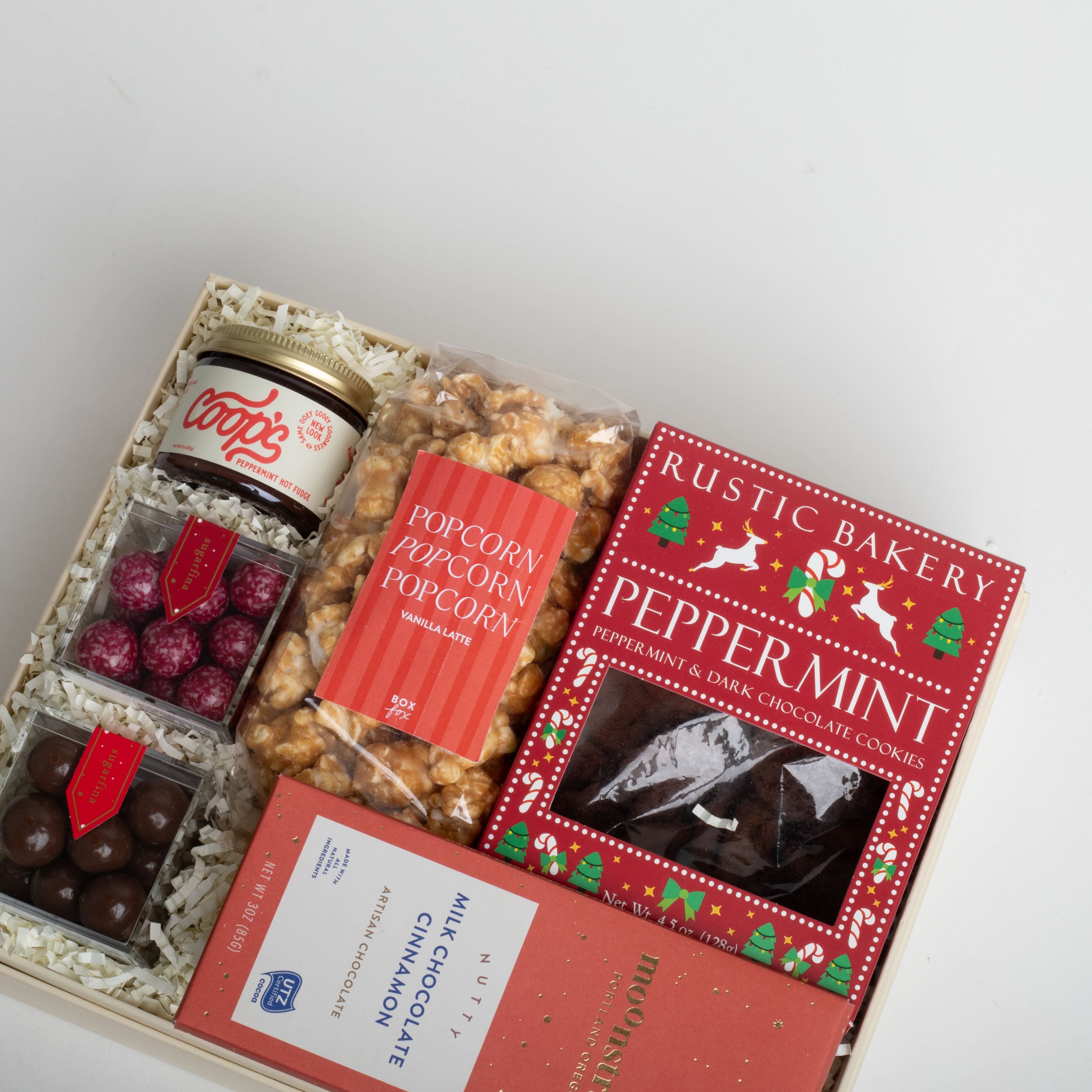 Gift box with snacks including peppermint cookies, popcorn, and chocolates on a light gray background