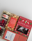 Gift box with snacks including peppermint cookies, popcorn, and chocolates on a light gray background