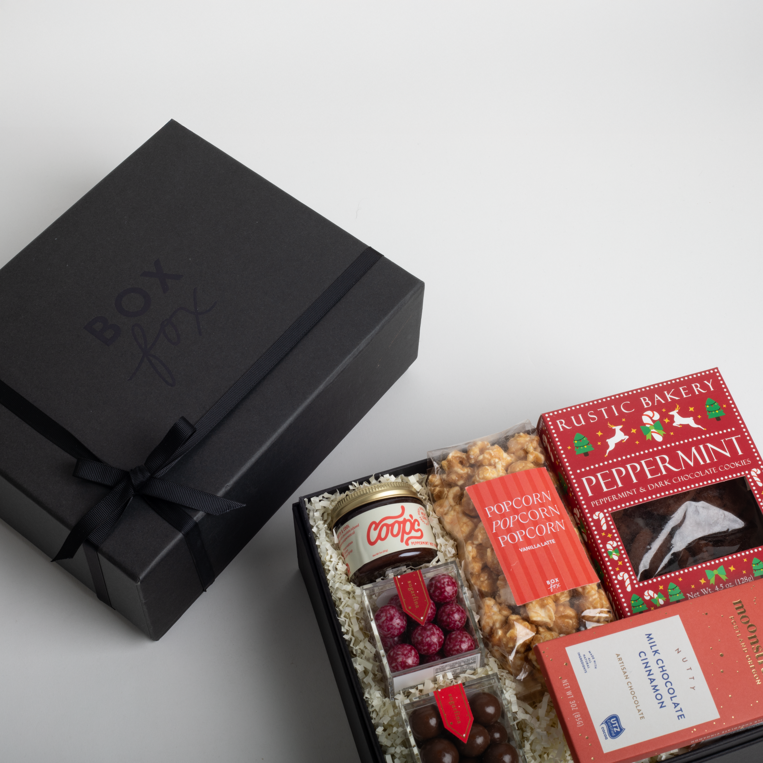 Gift box with assorted treats including cookies, popcorn, and chocolate on a light gray background