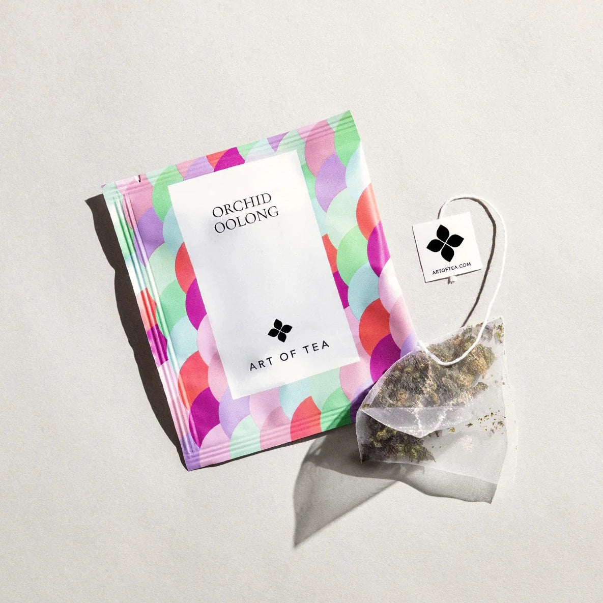 pastel colored tea sachet with. varies hues of purple, blue & green. next to it is a tea bag