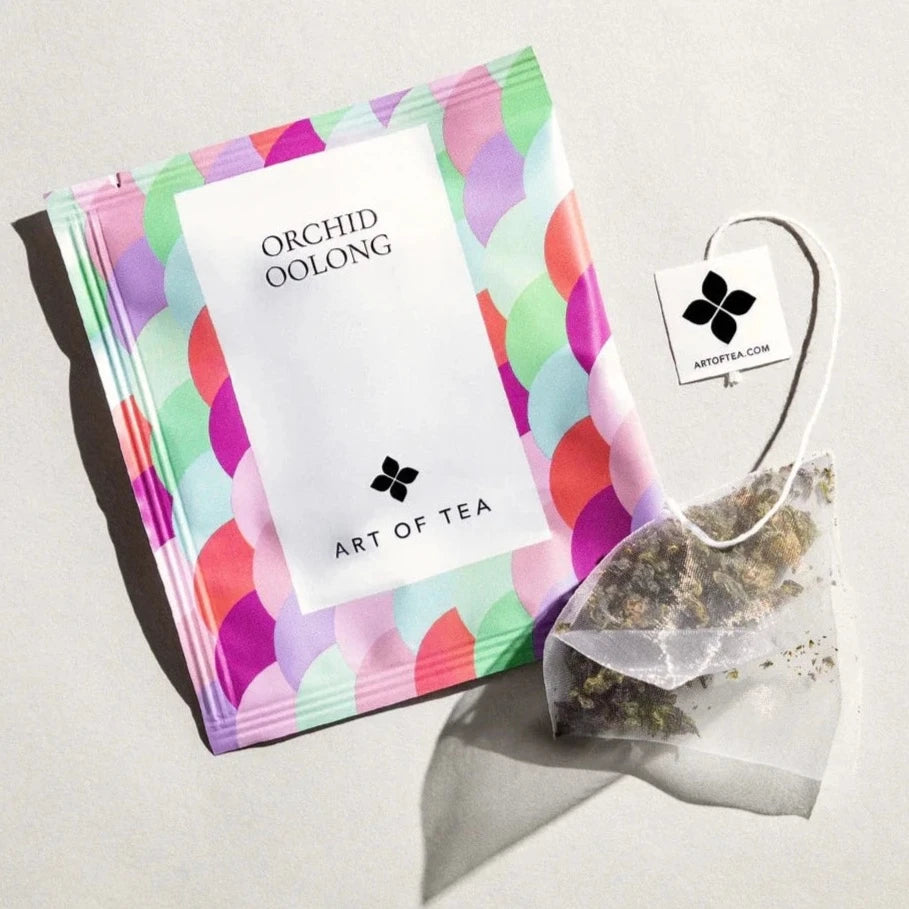 pastel colored tea sachet with. varies hues of purple, blue &amp; green. next to it is a tea bag