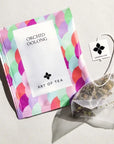 pastel colored tea sachet with. varies hues of purple, blue & green. next to it is a tea bag