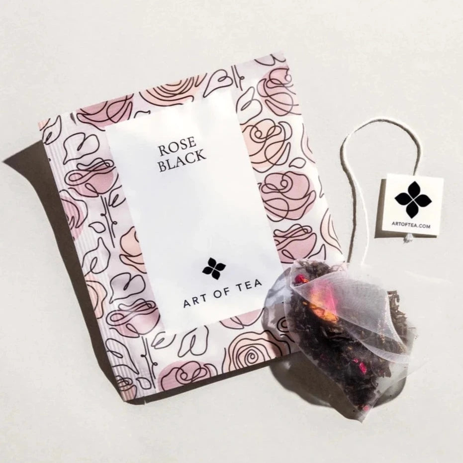 Rose Black tea sachet. Sachet has doodles of roses all over it and sachet is a very pale pink. Each doodled rose has a various shade of pink. Tea bag is outside the sachet
