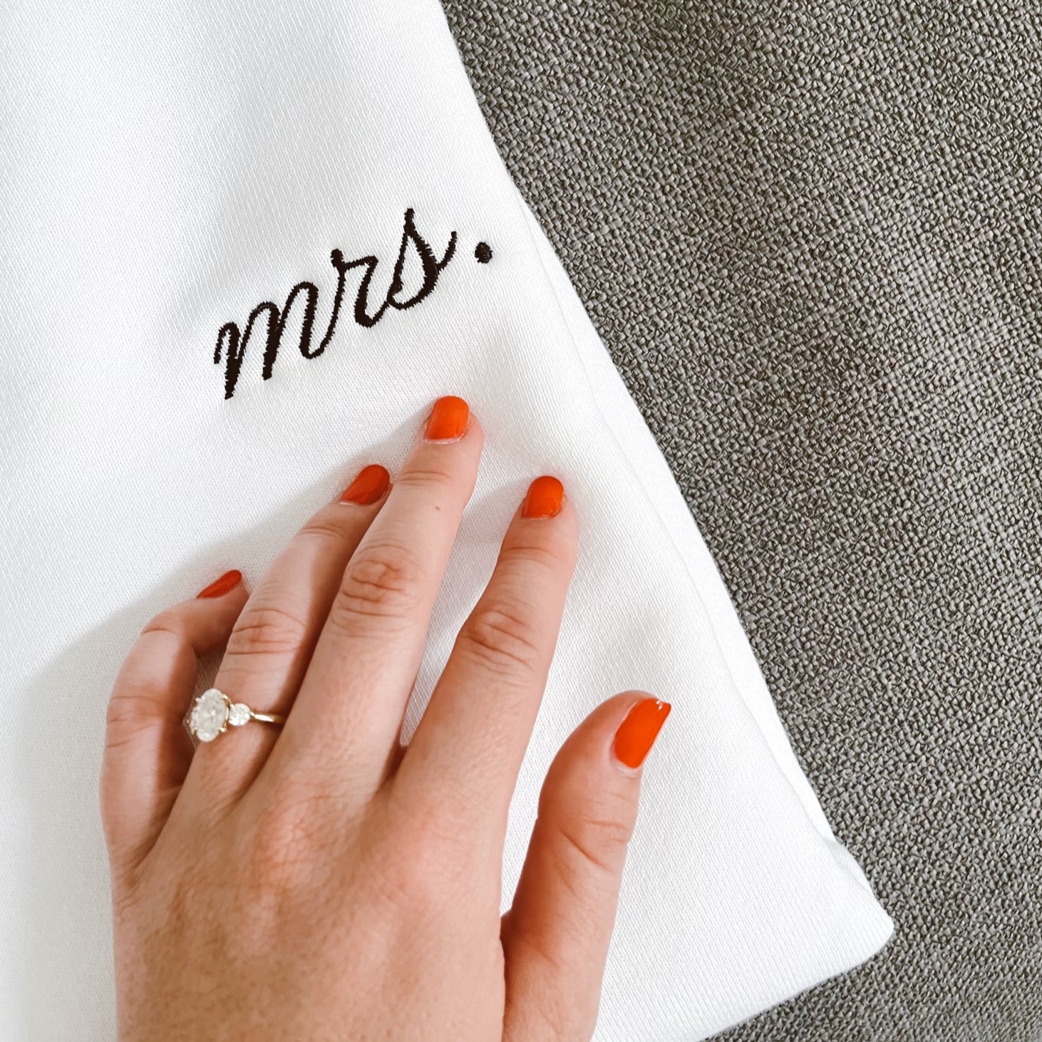 Hand with engagement ring rests on white Mrs. sweatshirt.