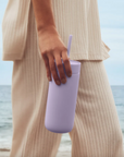 Woman at beach holds purple tumbler.