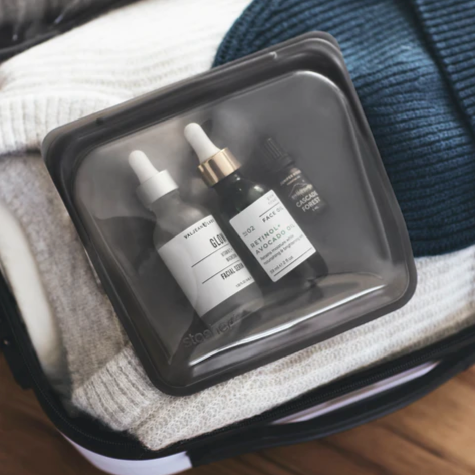 stasher bag filled with beauty products on clothes in a suitcase