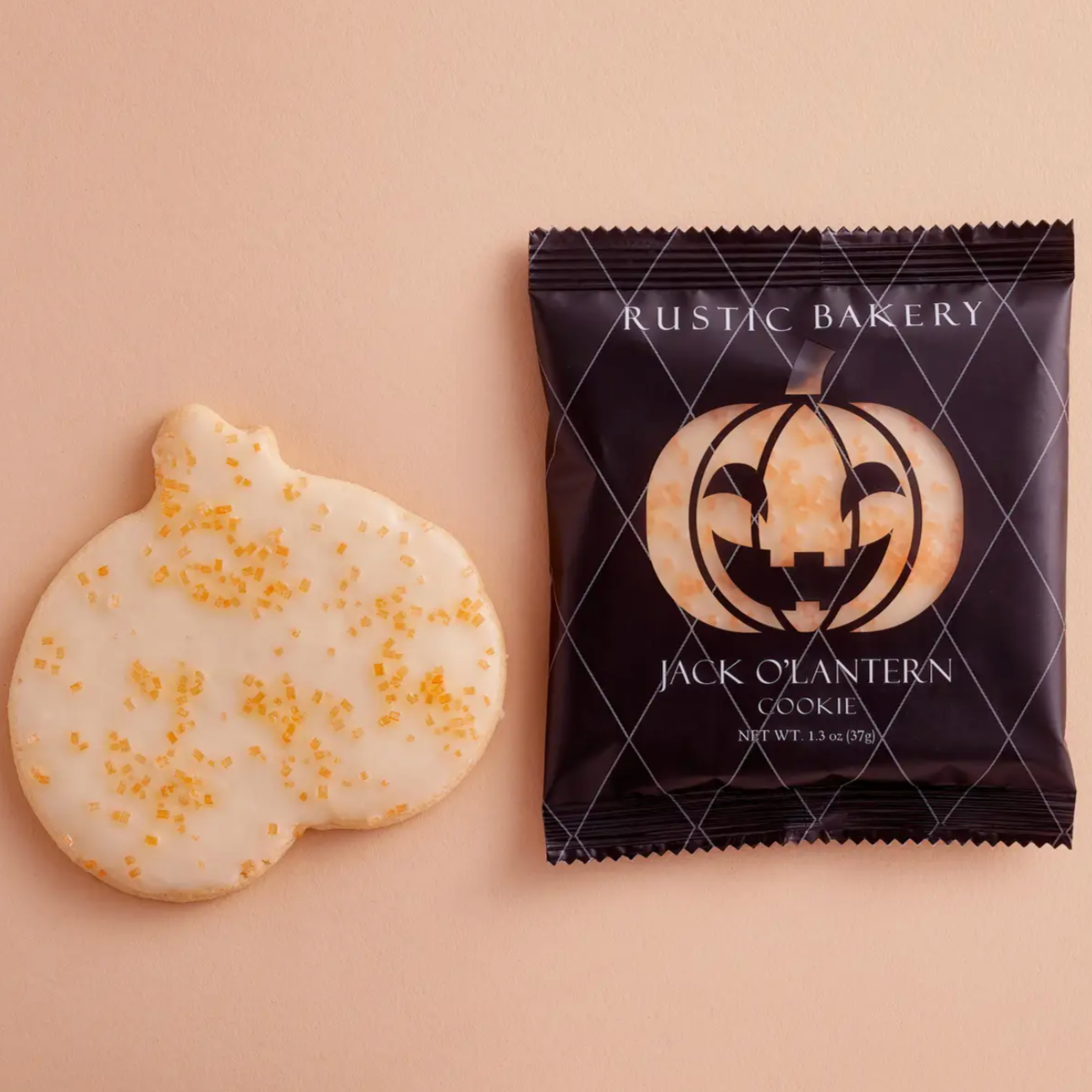 white frosted pumpkin cookie with orange sprinkles next to black and orange packaging behind pale orange background 