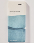 A chocolate bar in blue and white packaging on a white background that reads, "MAST Organic Dark Chocolate with Sea Salt"