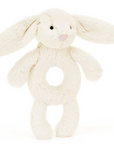 cream off white bunny stuffed animal rattle with hole in the middle behind white background 