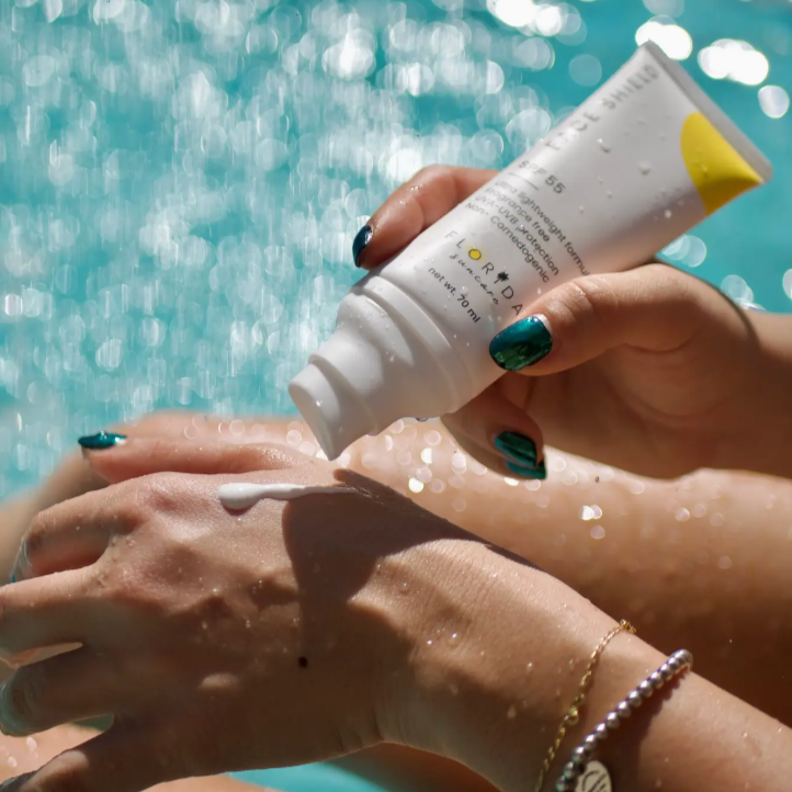 The sunscreen is shown being applied on a hand. The background is water.