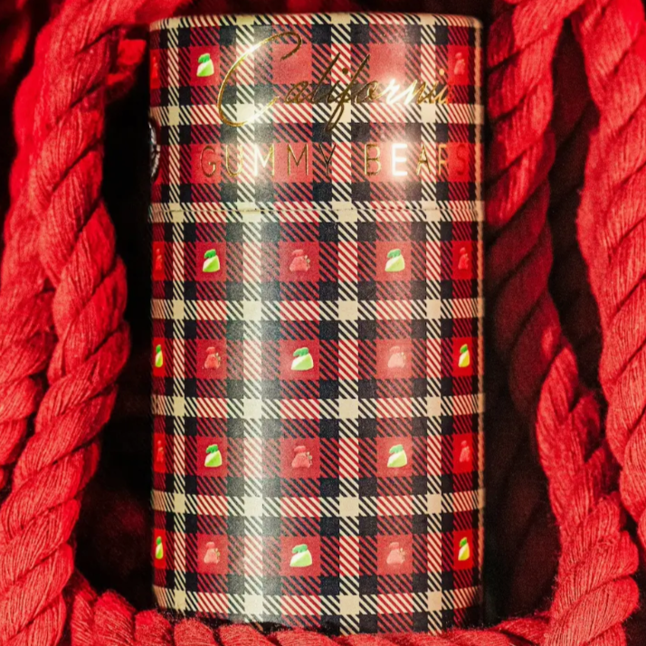 The brand "CALIFORNIA GUMMY BEARS" is written in gold on red, black and white plaid packaging, it also has strawberries and green apples on the plaid. The background is red ropes.