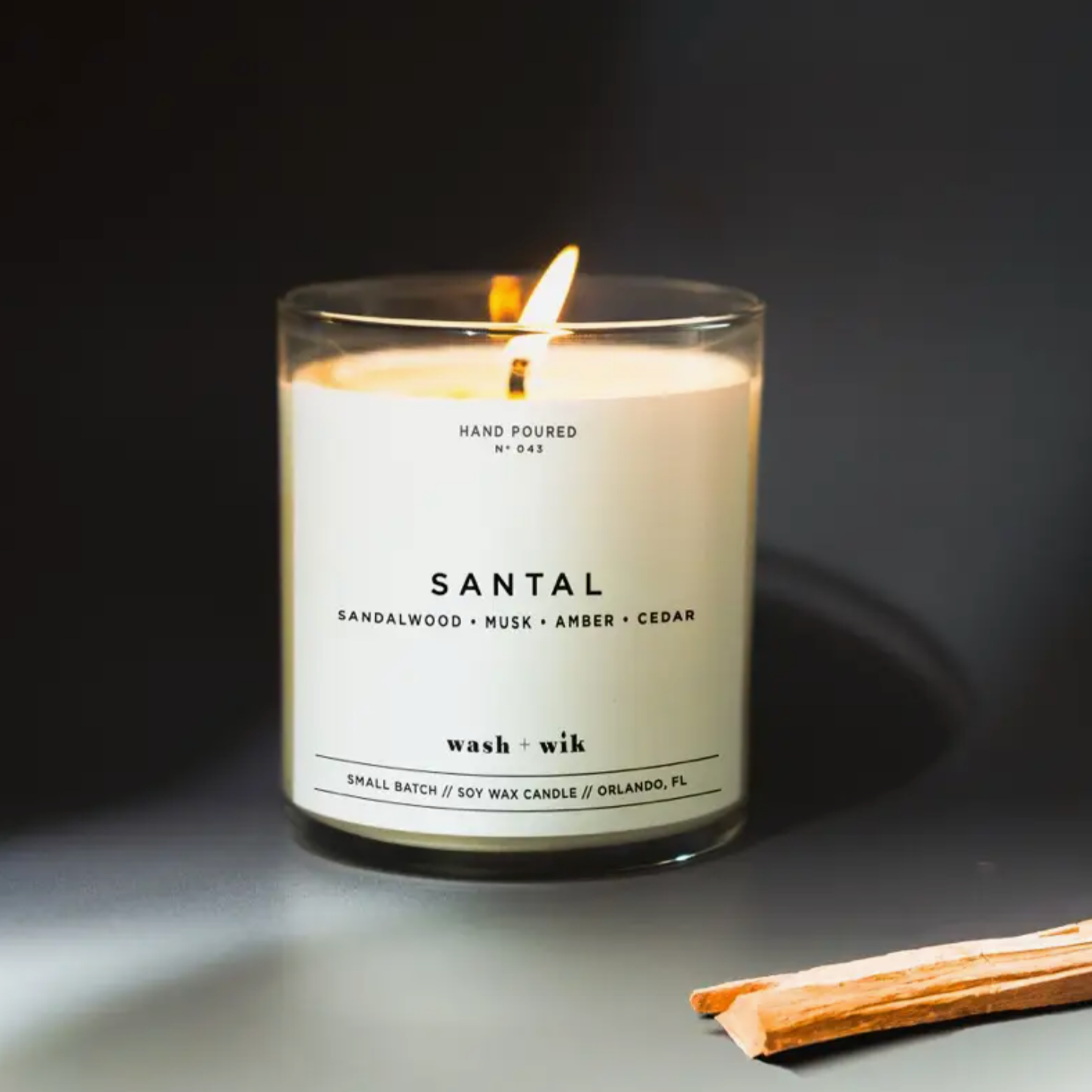 Wash + Wik Candle is shown lit in the scent "SANTAL" on a black background