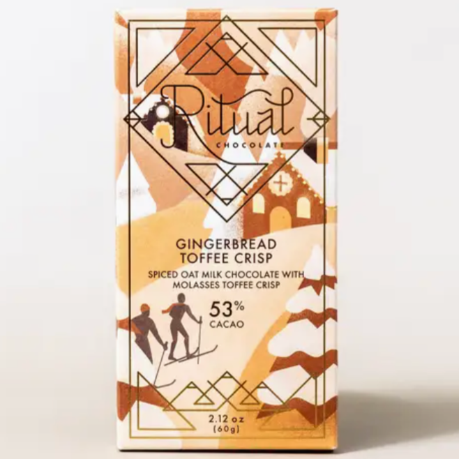 The image shows a product from Ritual Chocolate, specifically the "Gingerbread Toffee Crisp" bar. The packaging is decorated with festive gingerbread house and snow-like patterns in shades of brown and beige. The text on the front of the box reads "Ritual Chocolate" in an elegant script, with the flavor labeled as "Gingerbread Toffee Crisp" below. It is described as "Spiced Oat Milk Chocolate with Molasses Toffee Crisp" and contains 53% cacao. The packaging also indicates a weight of 2.12 oz (60g).  