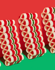 The image shows rows of neatly stacked cinnamon candy bundles in a spiral shape, alternating in red, white, and green colors. The background is split diagonally, with a festive red upper half and a green lower half, complementing the holiday-themed colors of the candy. 