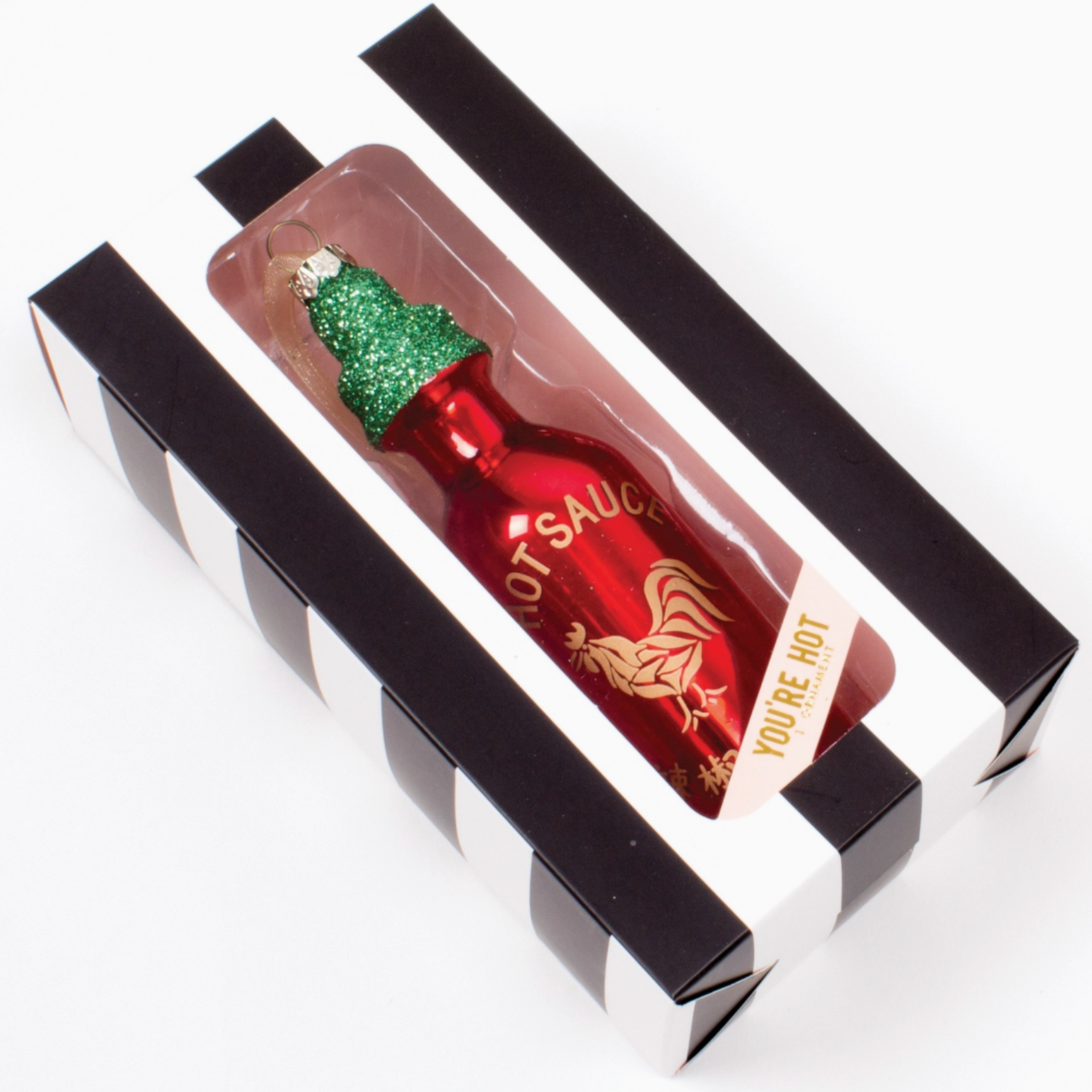 glass red hot sauce ornament with glittery green cap in a black and white striped box with clear front that says you're hot 