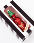 glass red hot sauce ornament with glittery green cap in a black and white striped box with clear front that says you're hot 