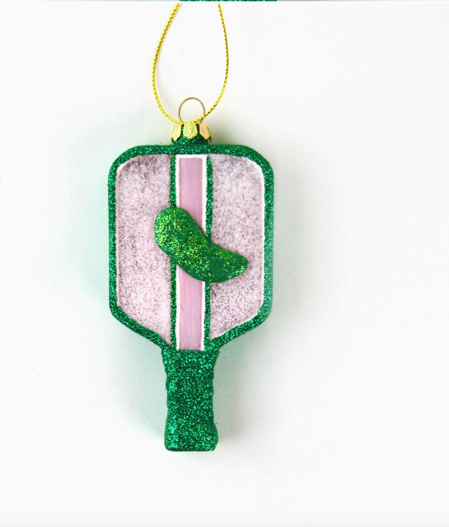 this image shows a pickleball racket shaped ornament, it is glittery with a green glittery pickle in the middle, green light pinks and whites are the main colors behind white background 