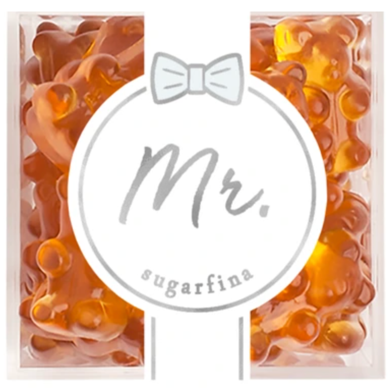 The image shows a package of gummy candies by Sugarfina. The packaging design has a label in the center with the text "Mr." written in a gray, cursive font. Above the text, there's a small, simple bow-tie graphic. Surrounding the label, the gummies are visible through the clear packaging. The gummies are amber-colored and shaped like bears.
