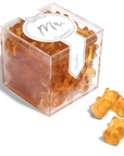 The image shows a package of gummy candies by Sugarfina. The packaging design has a label in the center with the text "Mr." written in a gray, cursive font. Above the text, there's a small, simple bow-tie graphic. Surrounding the label, the gummies are visible through the clear packaging. The gummies are amber-colored and shaped like bears. There are three bears outside of the box pictured to the right of the box. 





