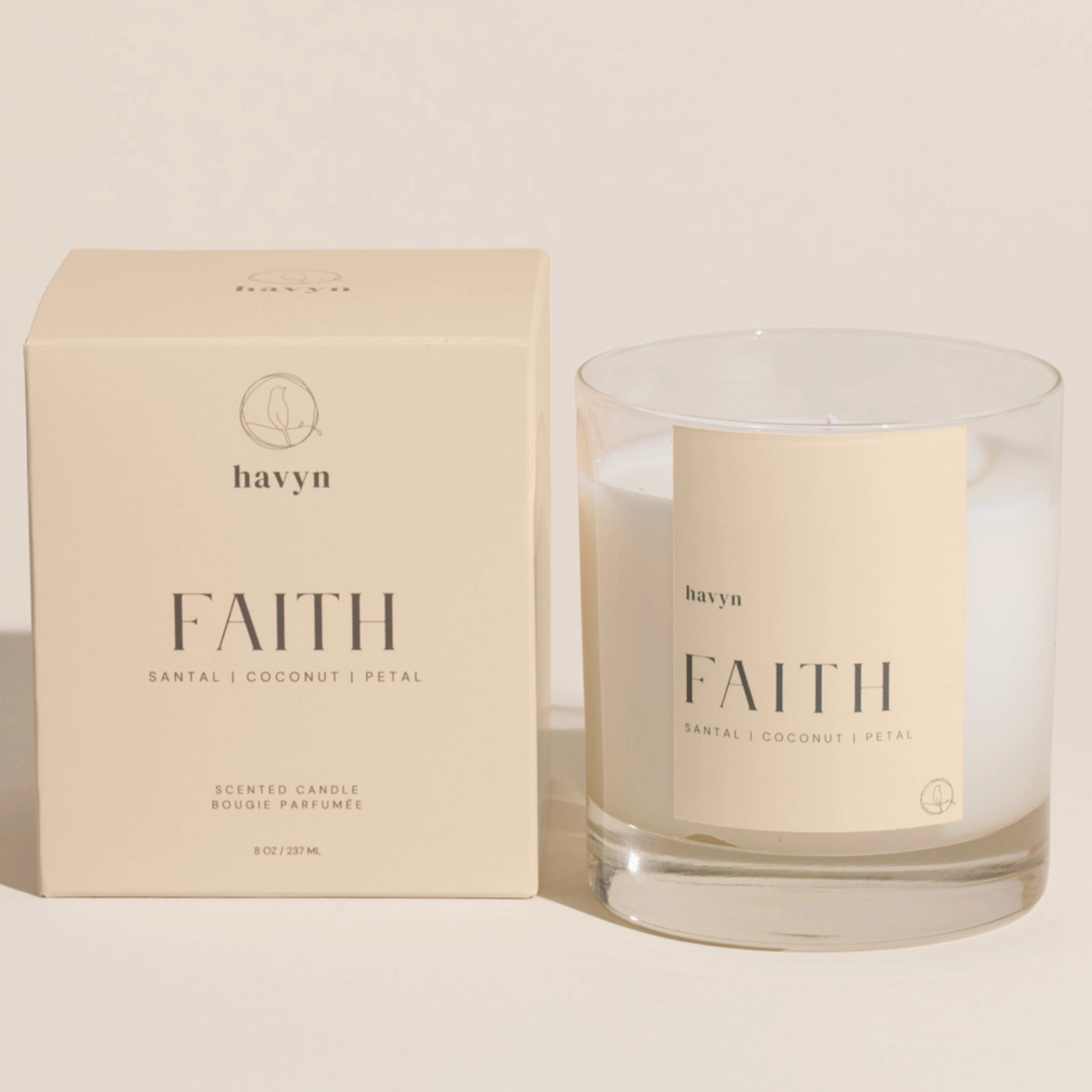 pale beige candle packaging by HAVYN that says FAITH SANTAL COCONUT PETAL next to clear glass candle on the right 