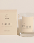 pale beige candle packaging by HAVYN that says FAITH SANTAL COCONUT PETAL next to clear glass candle on the right 