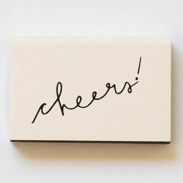 off white matchbox that says cheers! in handwritten script in black 