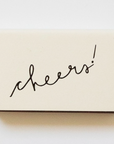 off white matchbox that says cheers! in handwritten script in black 